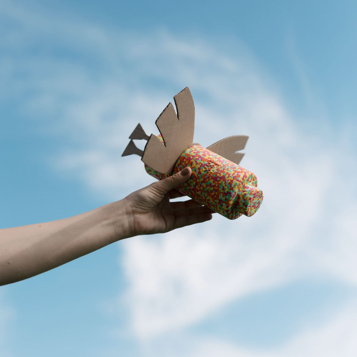 Hand hält bunten EPP-Baustein mit Cardboard-Flügeln als Vogel in den blauen Himmel.