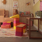 Kleinkind im Bett beobachtet bunte bygge XXL-Bausteine in Pink, Orange, Gelb – als Turm und Treppe aufgebaut im Kinderzimmer.