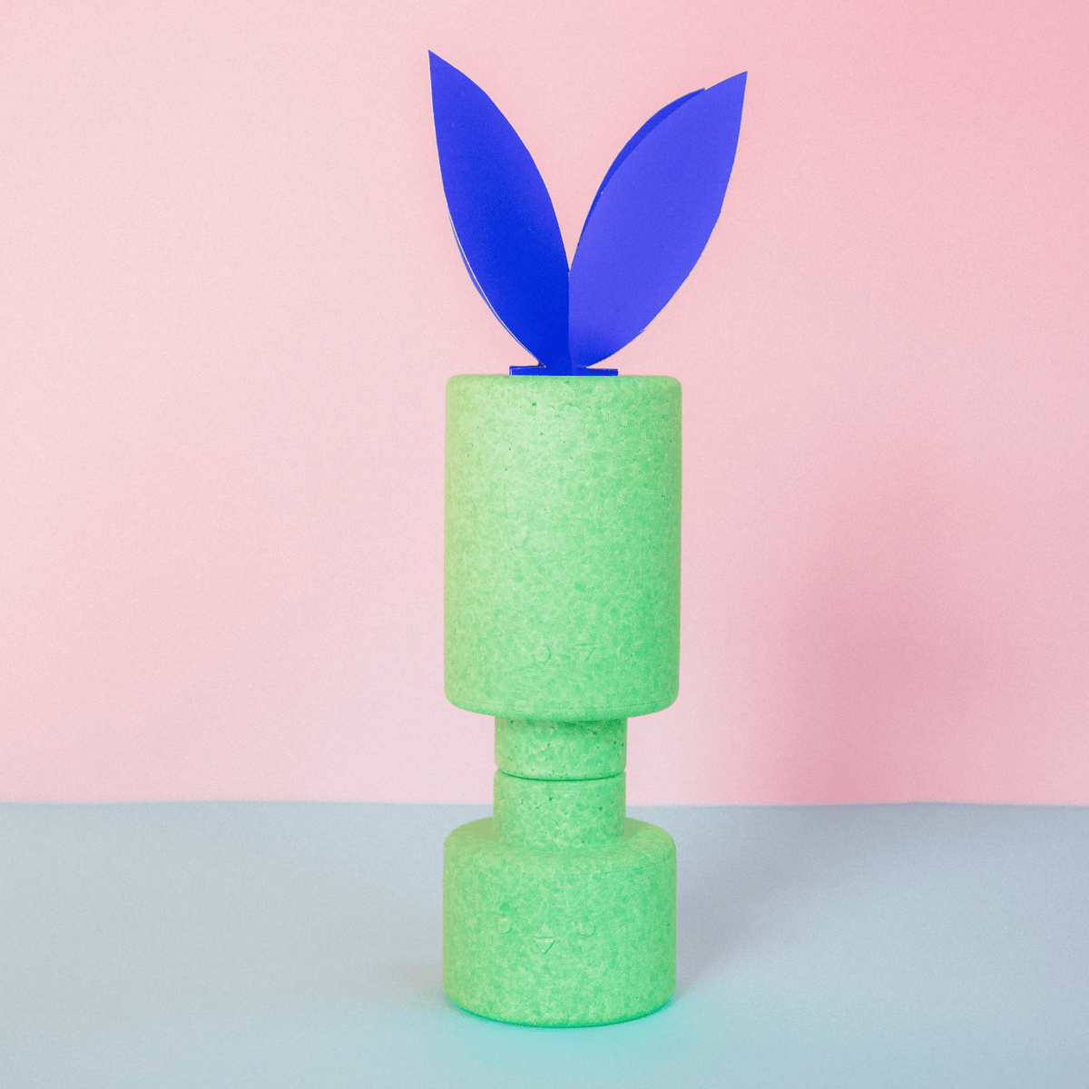 Grüne EPP-Bausteine XXL gestapelt als Turm, oben blaue Papier-Osterhasenohren, rosa Hintergrund.