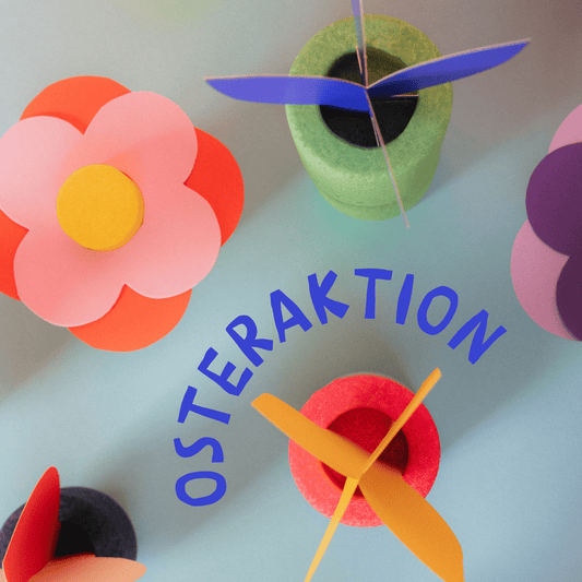 Bunte Papierblumen und EPP-Bausteine XXL auf hellblauem Untergrund mit Schriftzug „Osteraktion