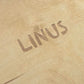 Nahaufnahme eines hellen Holzbretts mit eingefrästem Schriftzug „LINUS" in Großbuchstaben.