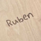 Name „Ruben" in geschwungener Schrift in helles Holz eingraviert – Nahaufnahme einer personalisierten Holzoberfläche.